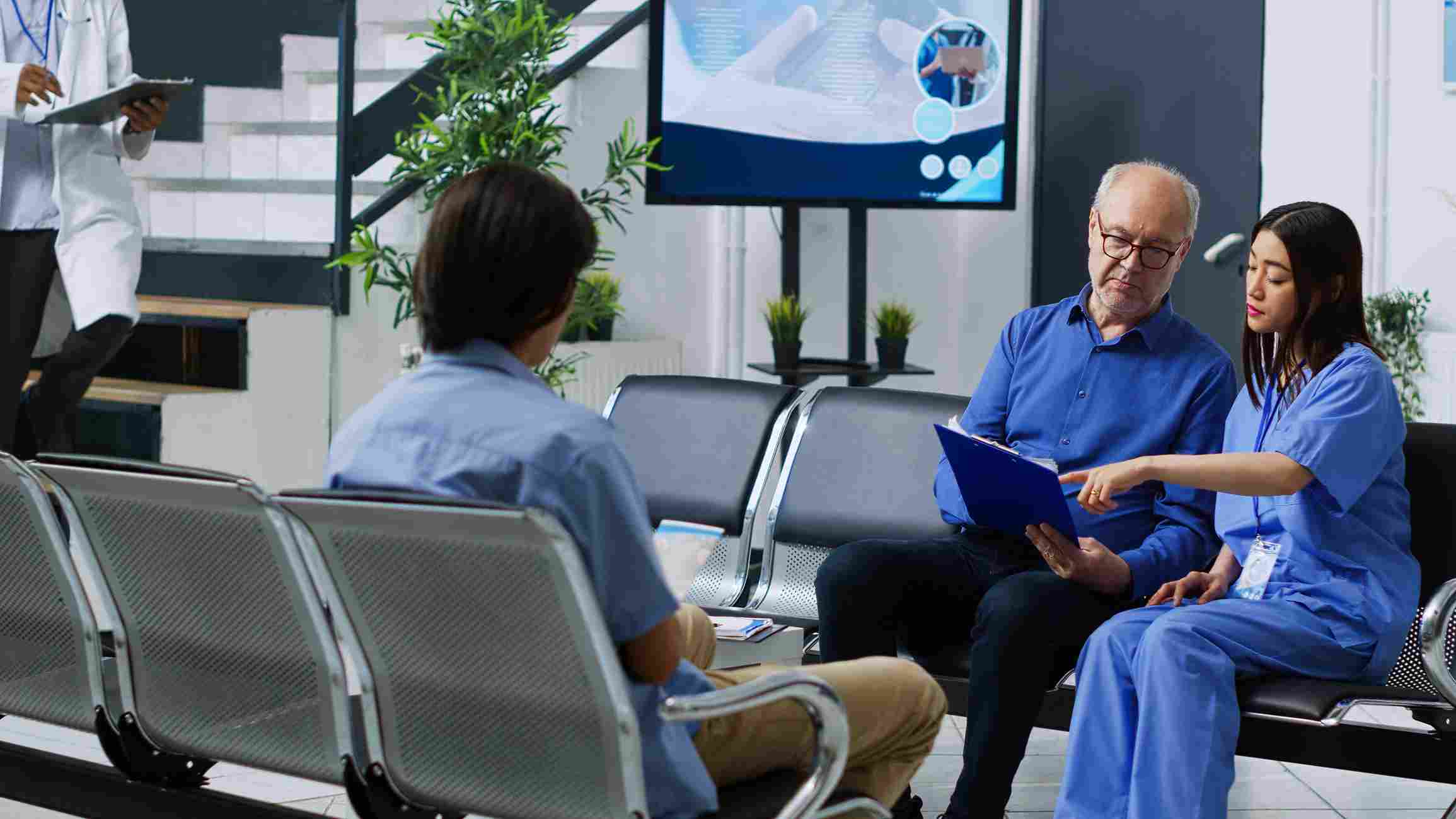 Medical staff explains hospital management software to a senior patient in a clinic.