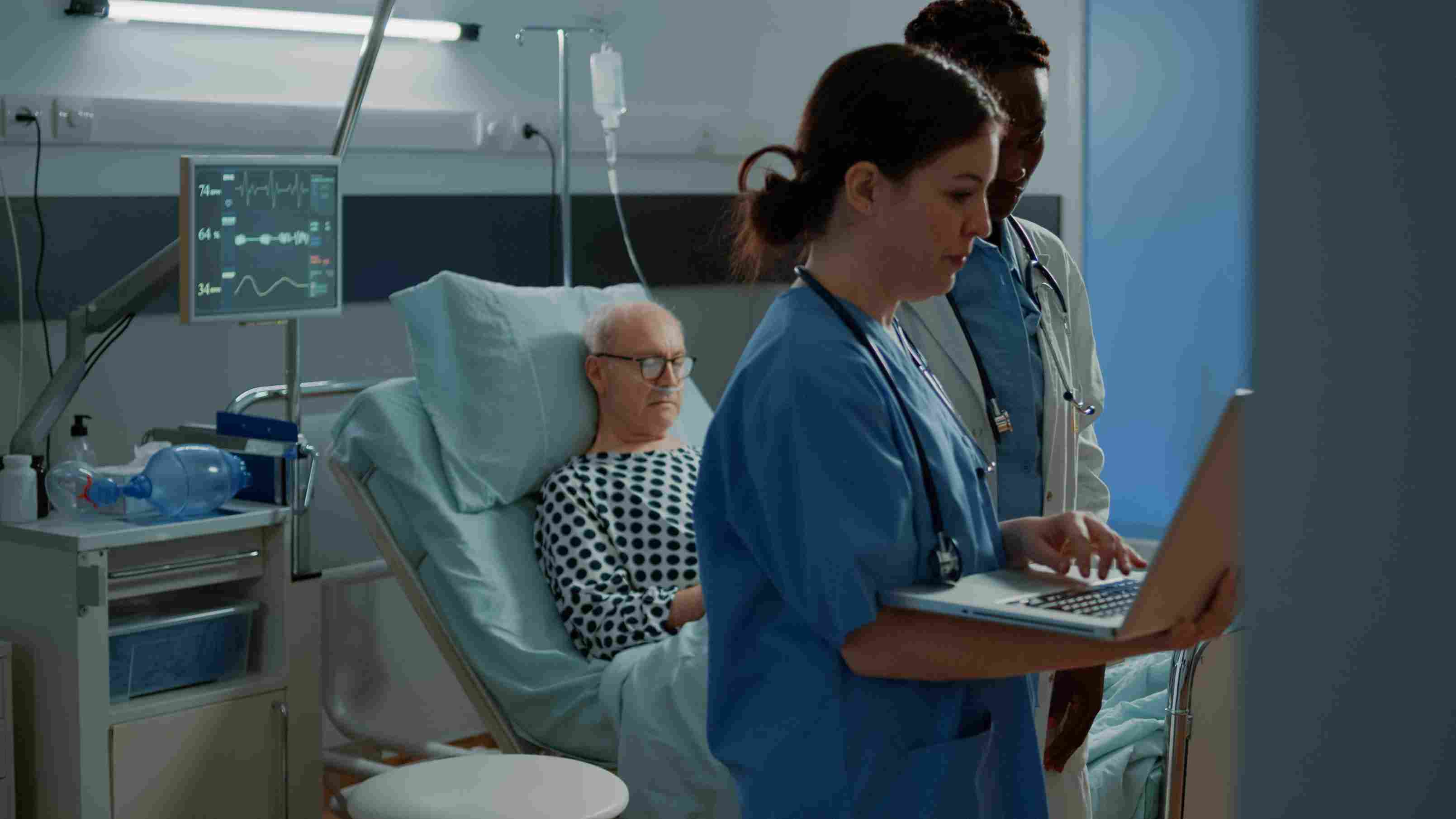 Hospital staff checks patient data using hospital management system at bedside.