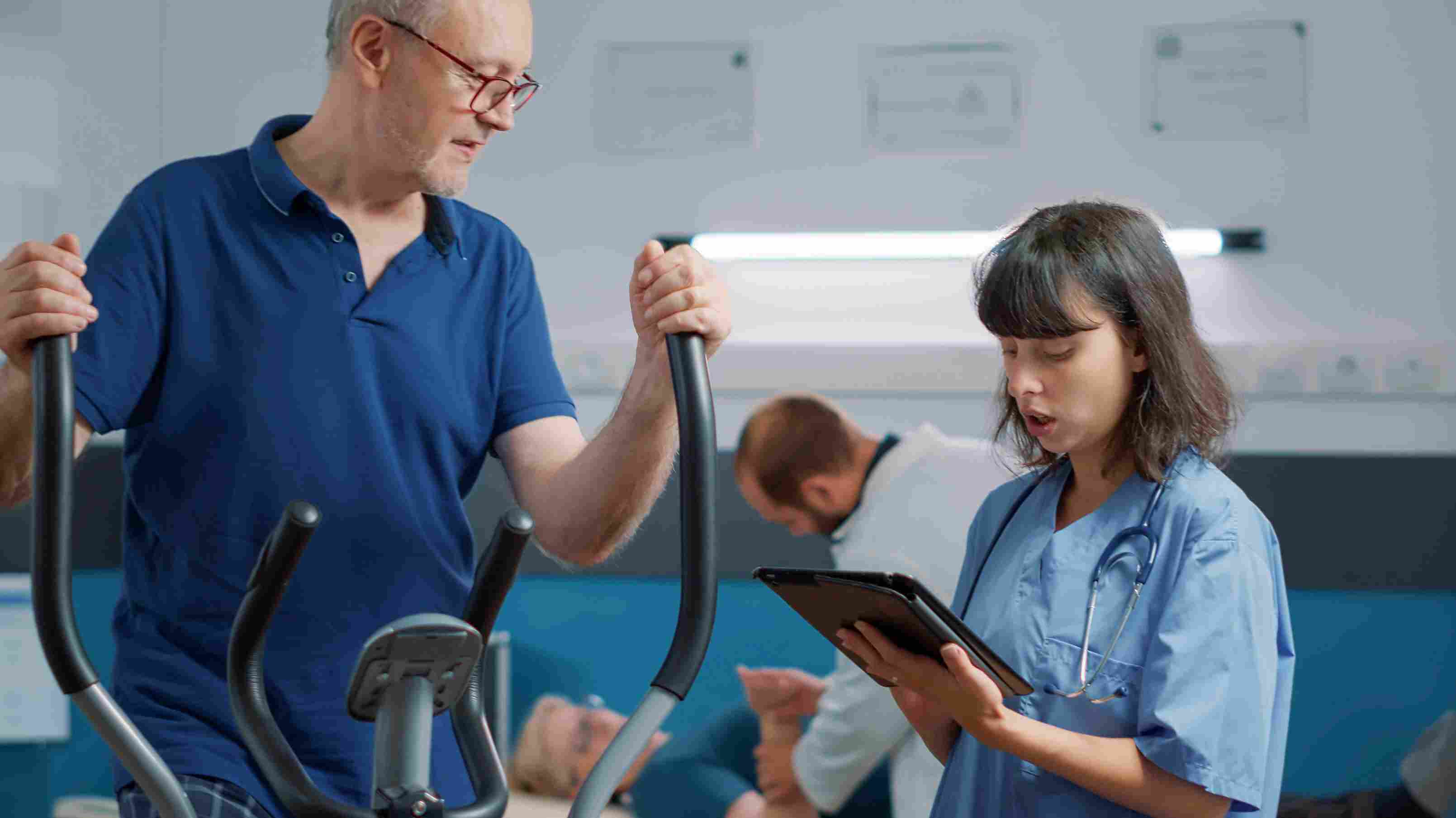 Nurse assisting an elderly patient on a stationary bike while discussing treatment details, demonstrating attentive patient care and rehabilitation support.