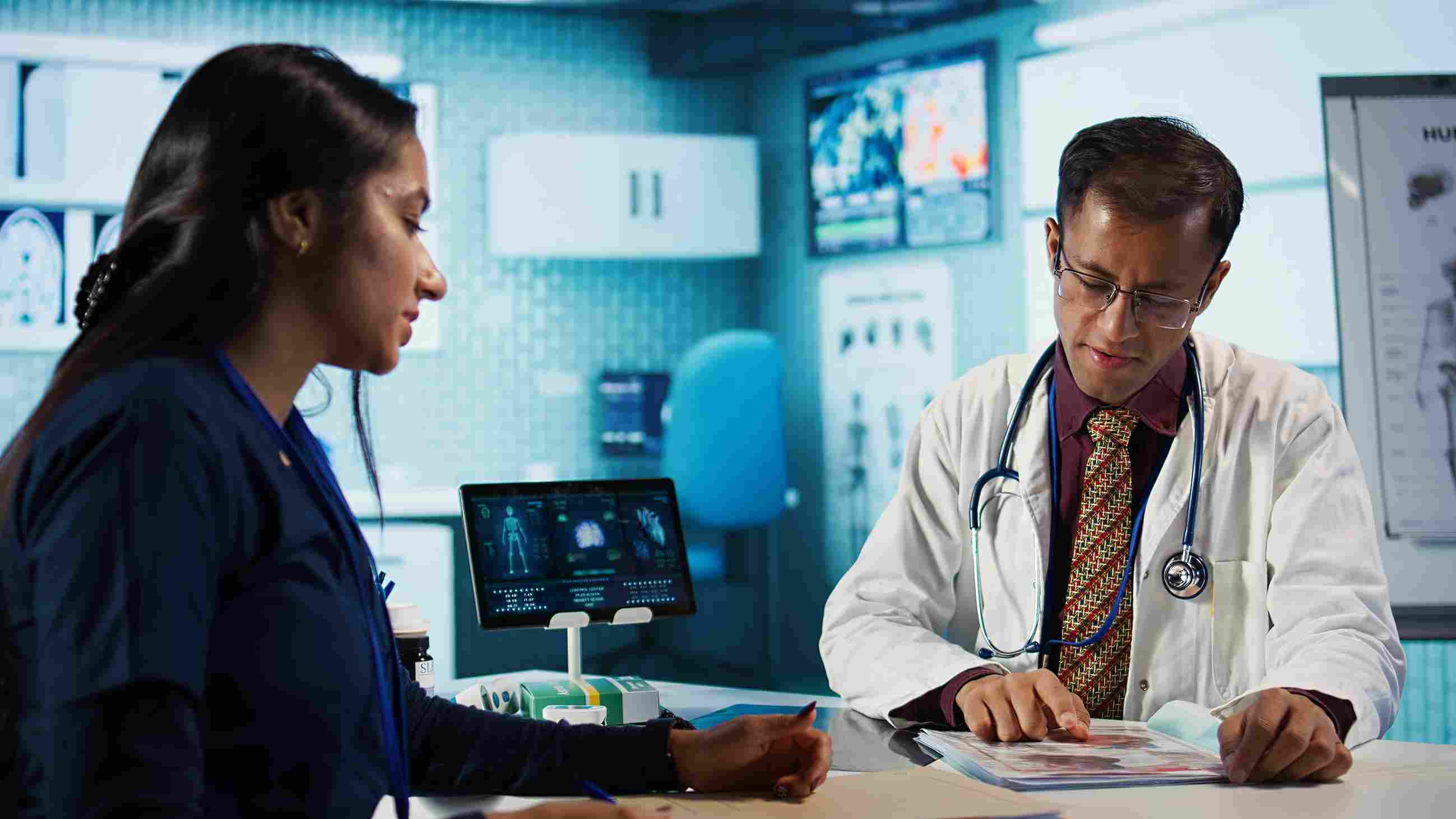 A doctor and nurse discussing patient reports in a modern hospital office with medical charts and digital monitors in the background