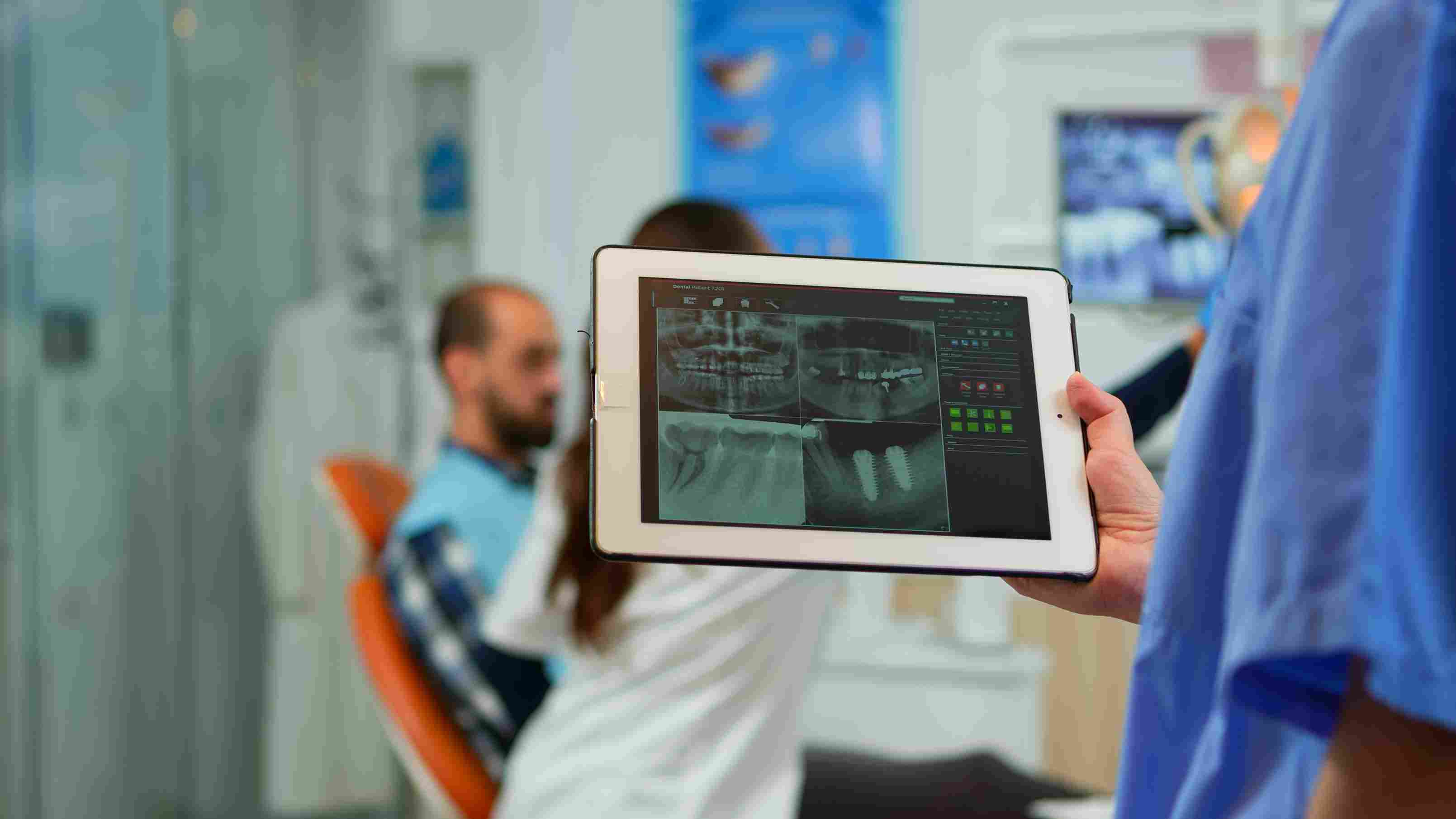 Doctor using hospital management software to view dental X-rays during patient consultation.