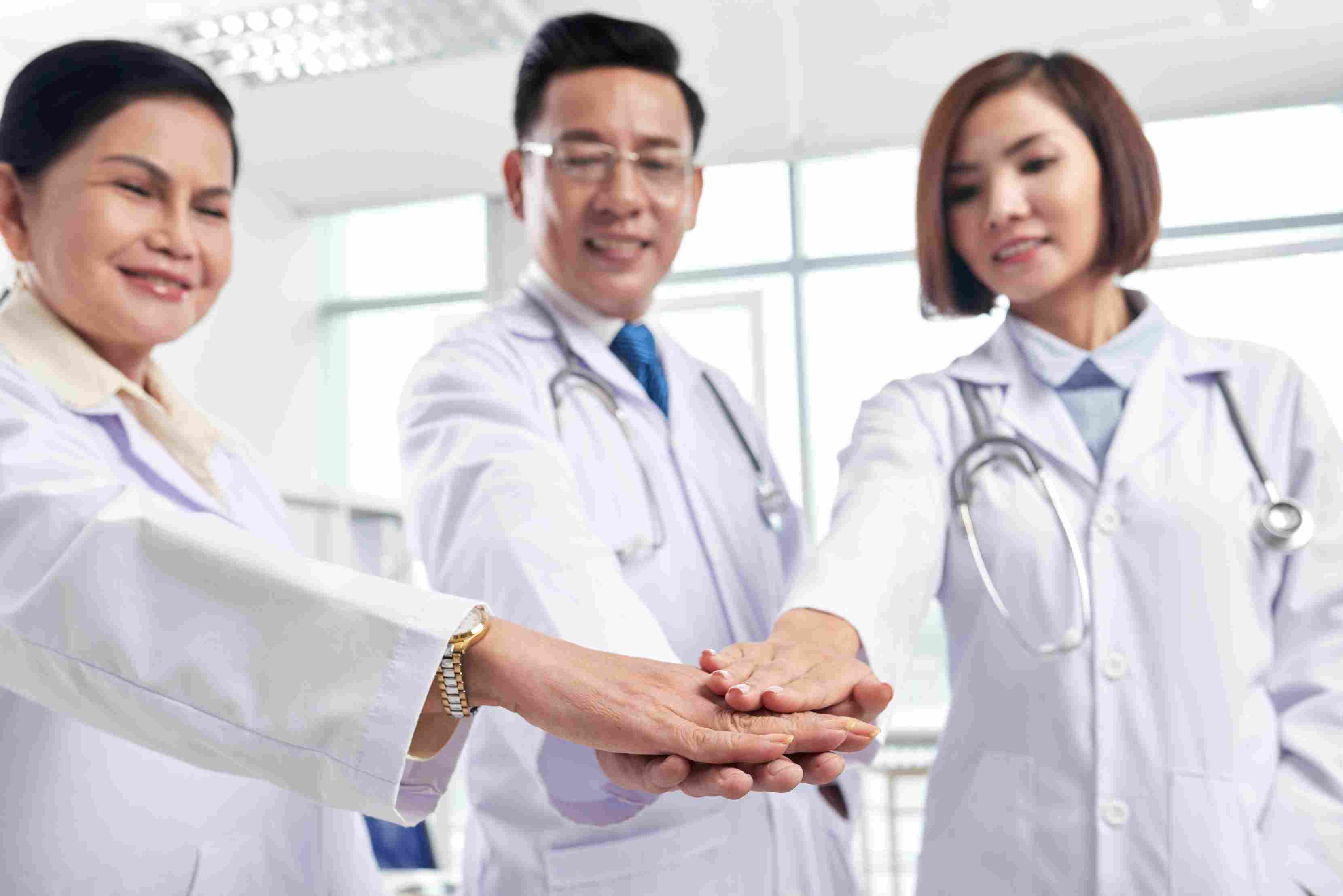 Three doctors wearing lab coats stack their hands to show teamwork and support, highlighting collaboration as a key success factor for digital transformation in Philippine healthcare