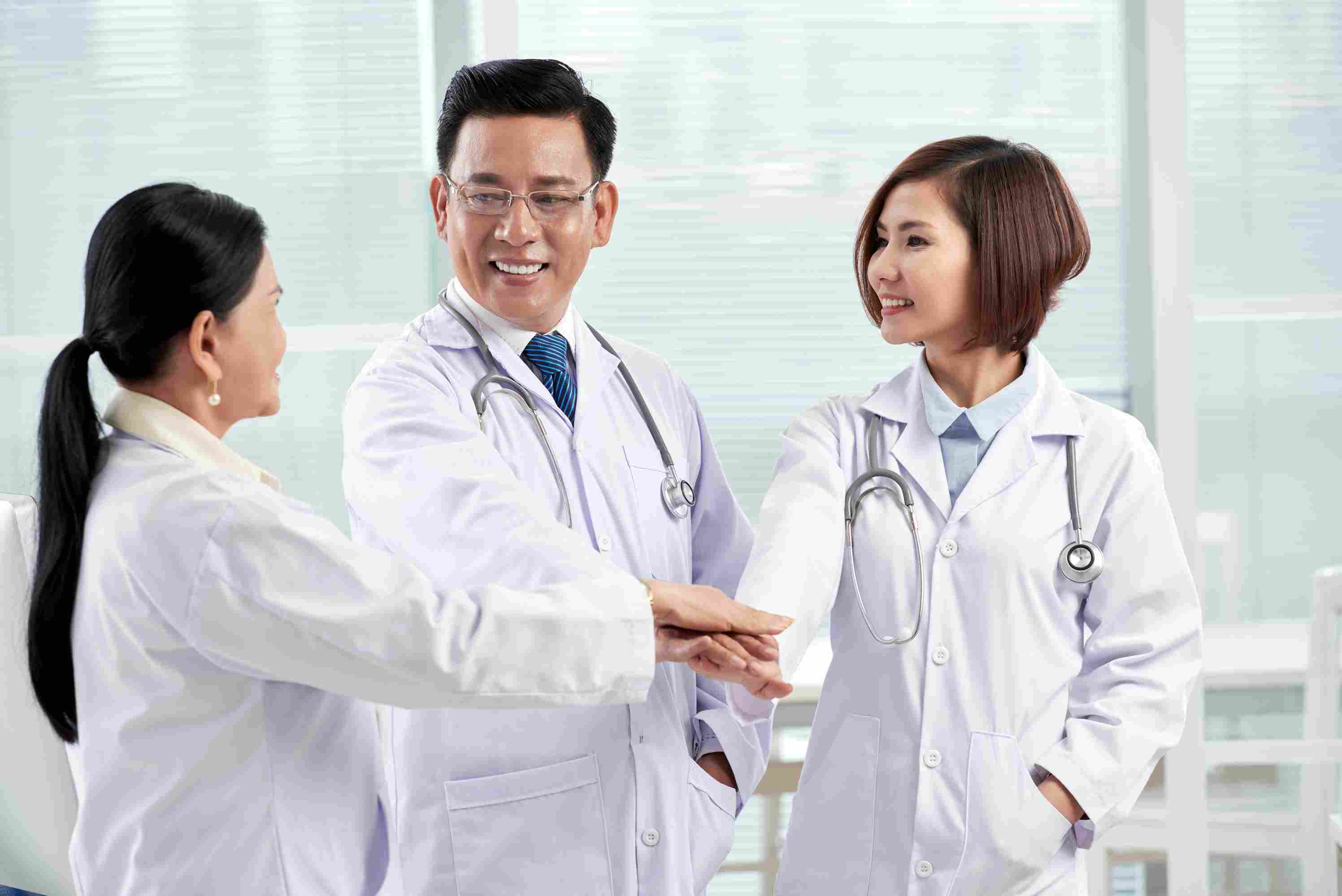 Three doctors in lab coats joining hands in a gesture of unity, symbolizing collaborative progress and digital integration for better healthcare in the Philippines