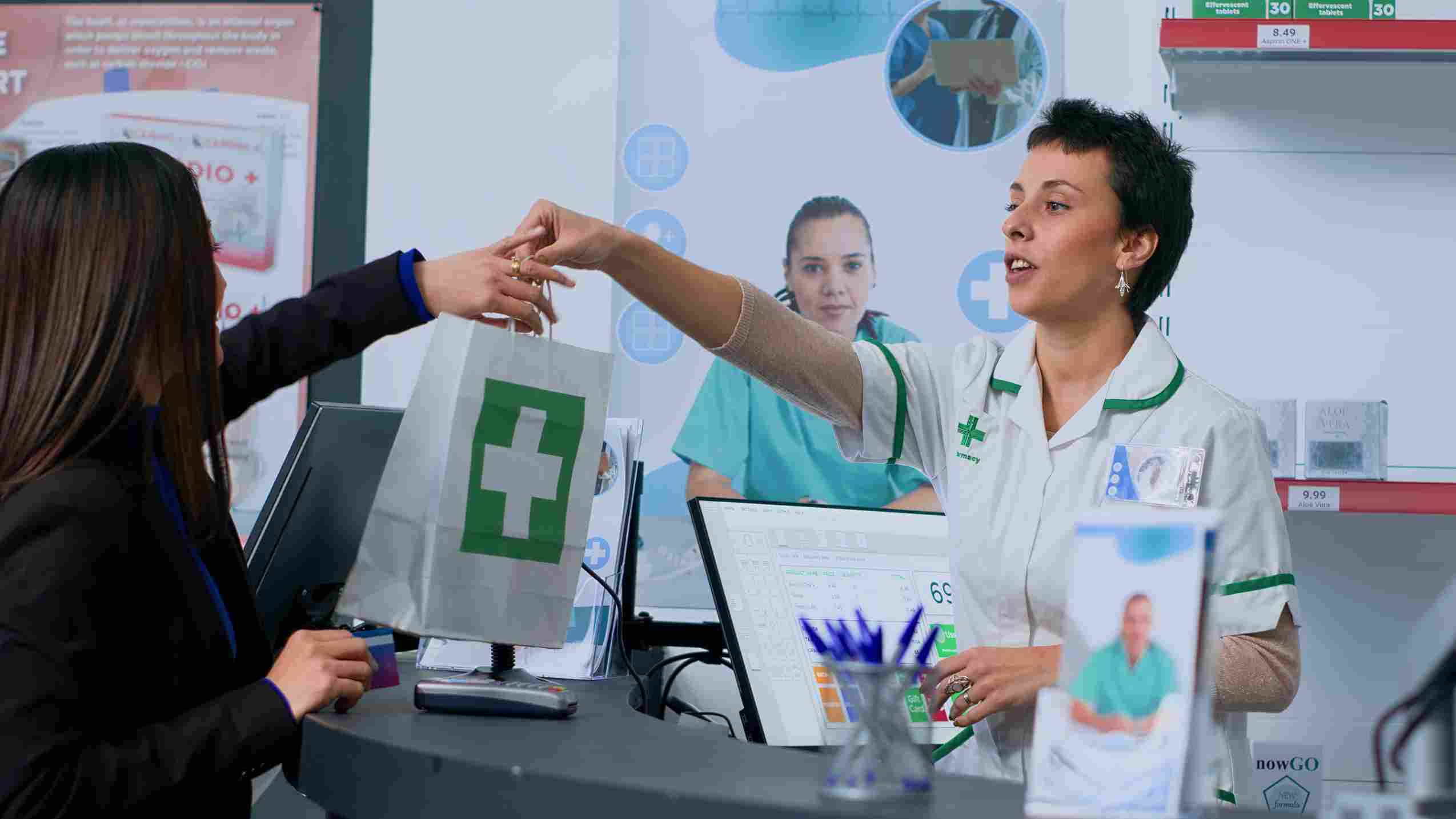 Pharmacy checkout counter with pharmacist handing over a bag and customer paying via card, reflecting HMS-enabled seamless billing and inventory updates.