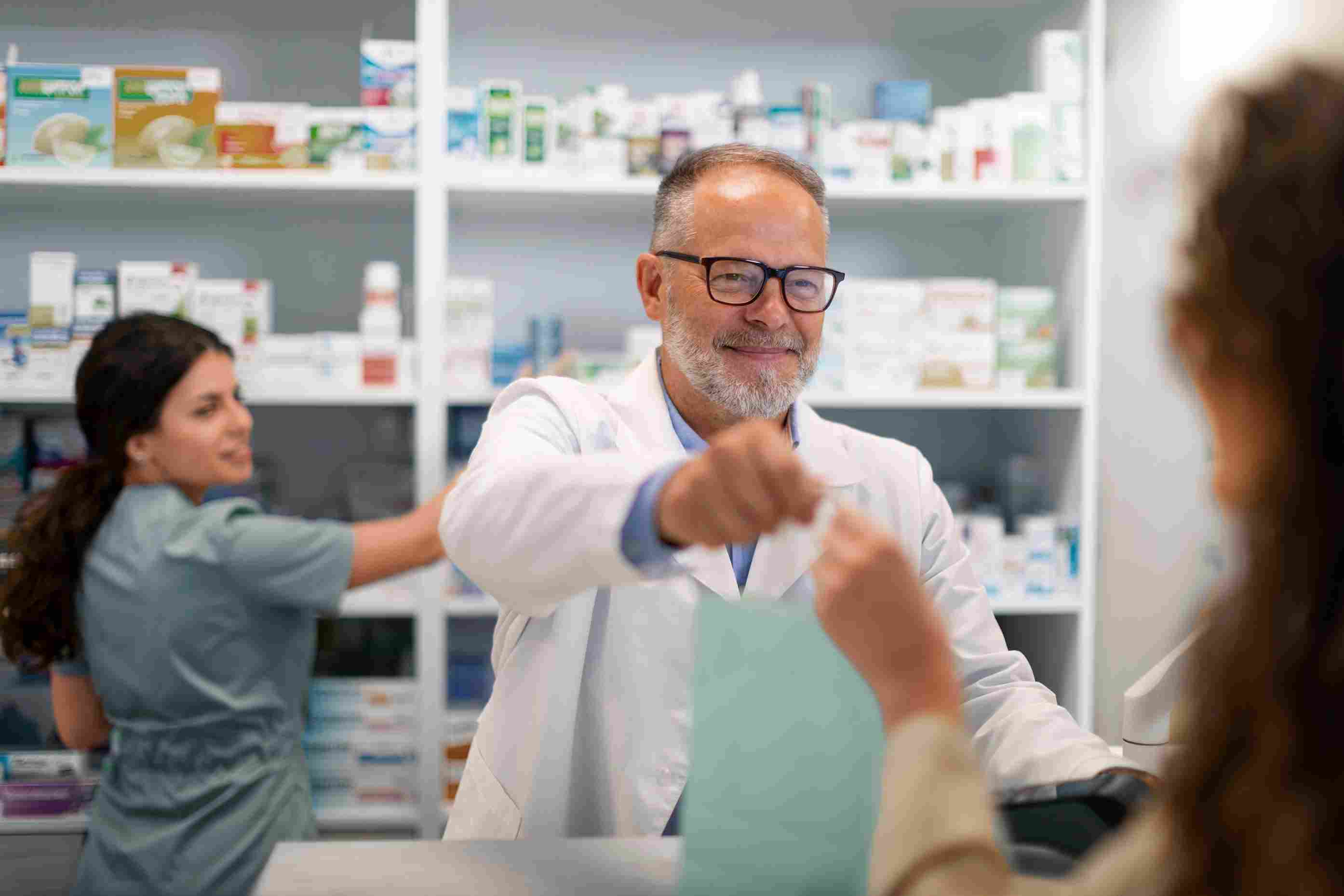 Senior pharmacist smiling while handing over prescription medicine, showcasing how HMS improves dispensing accuracy and boosts customer satisfaction.