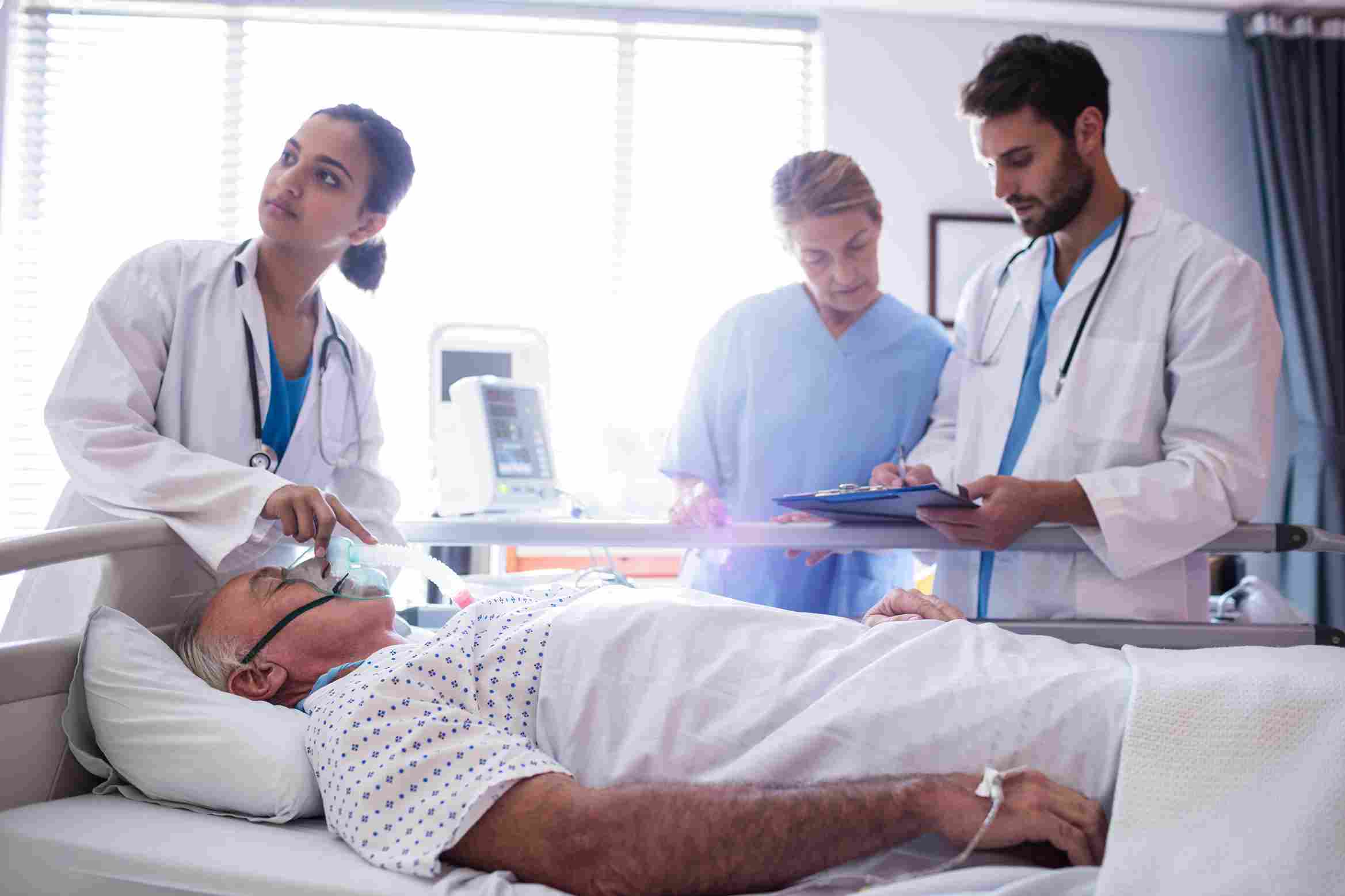 Doctor assisting an elderly patient with oxygen while medical staff review health records, showcasing how EMR/EHR improves patient care and safety in hospitals.