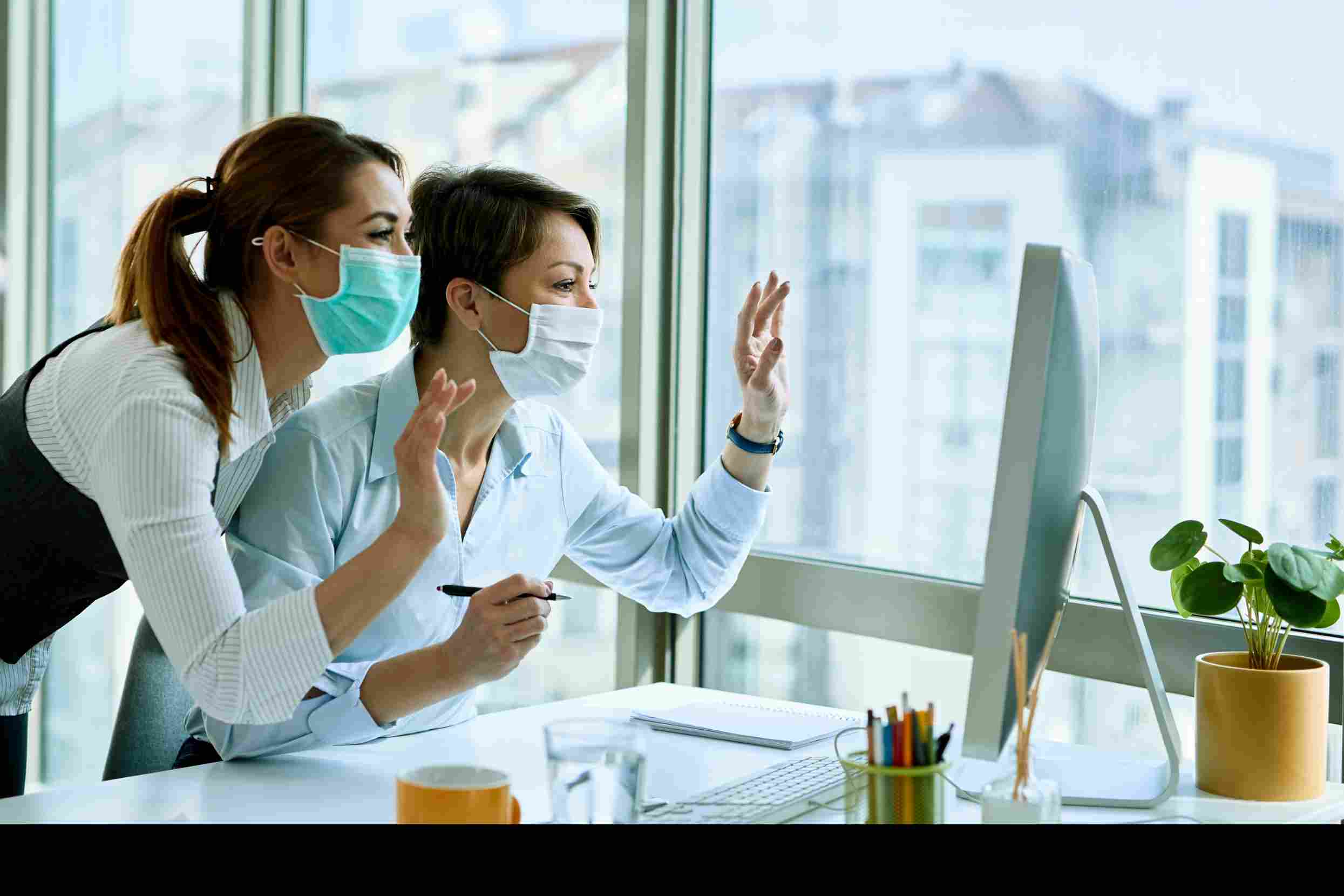 Businesswomen wearing masks making a video call, symbolizing how EMR/EHR and patient portals enable secure communication and greater engagement in healthcare.