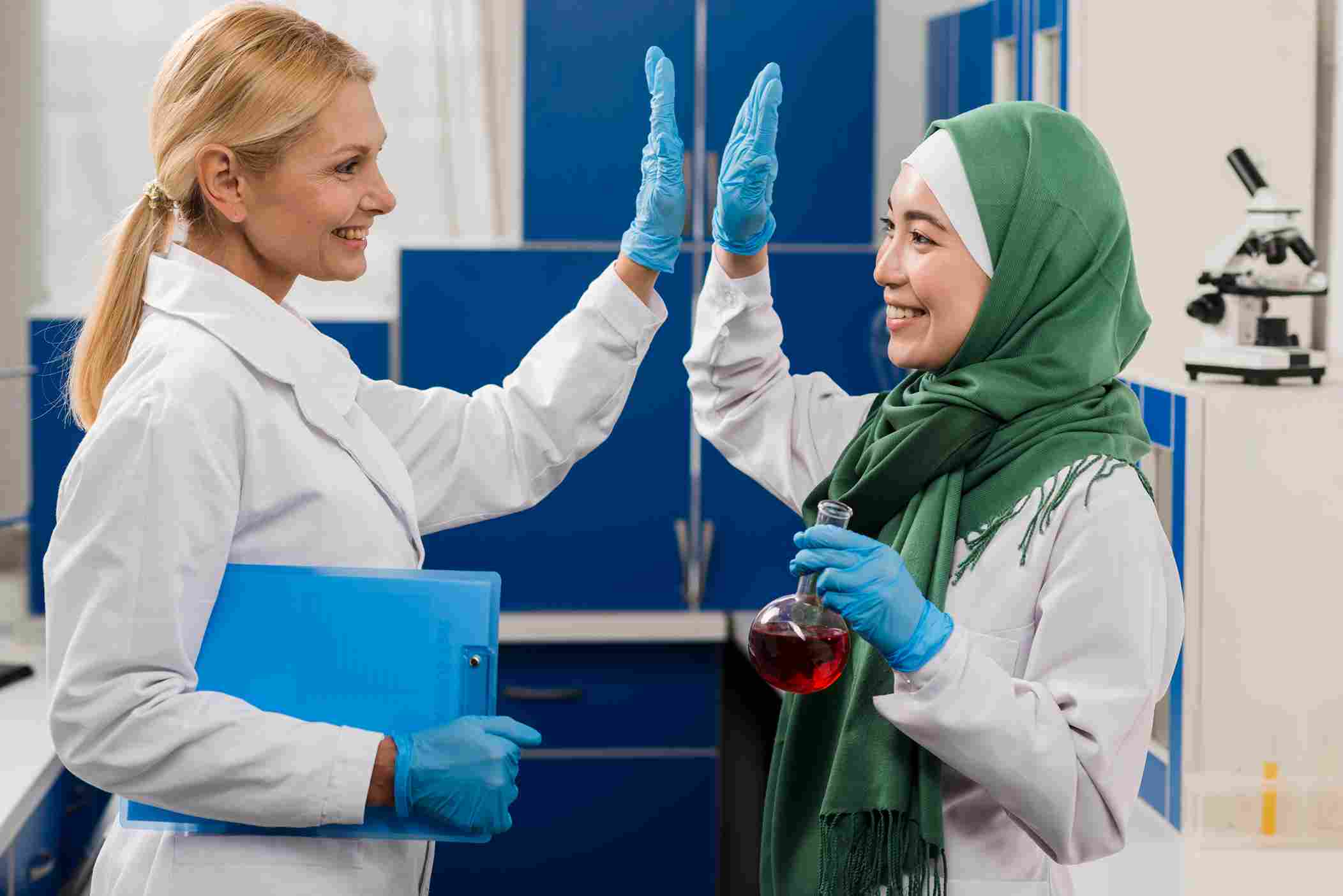 Two female lab scientists in medical attire celebrating with a high-five, representing collaboration and successful adoption of interoperable Health Information Exchange and Hospital Management Systems for better patient outcomes