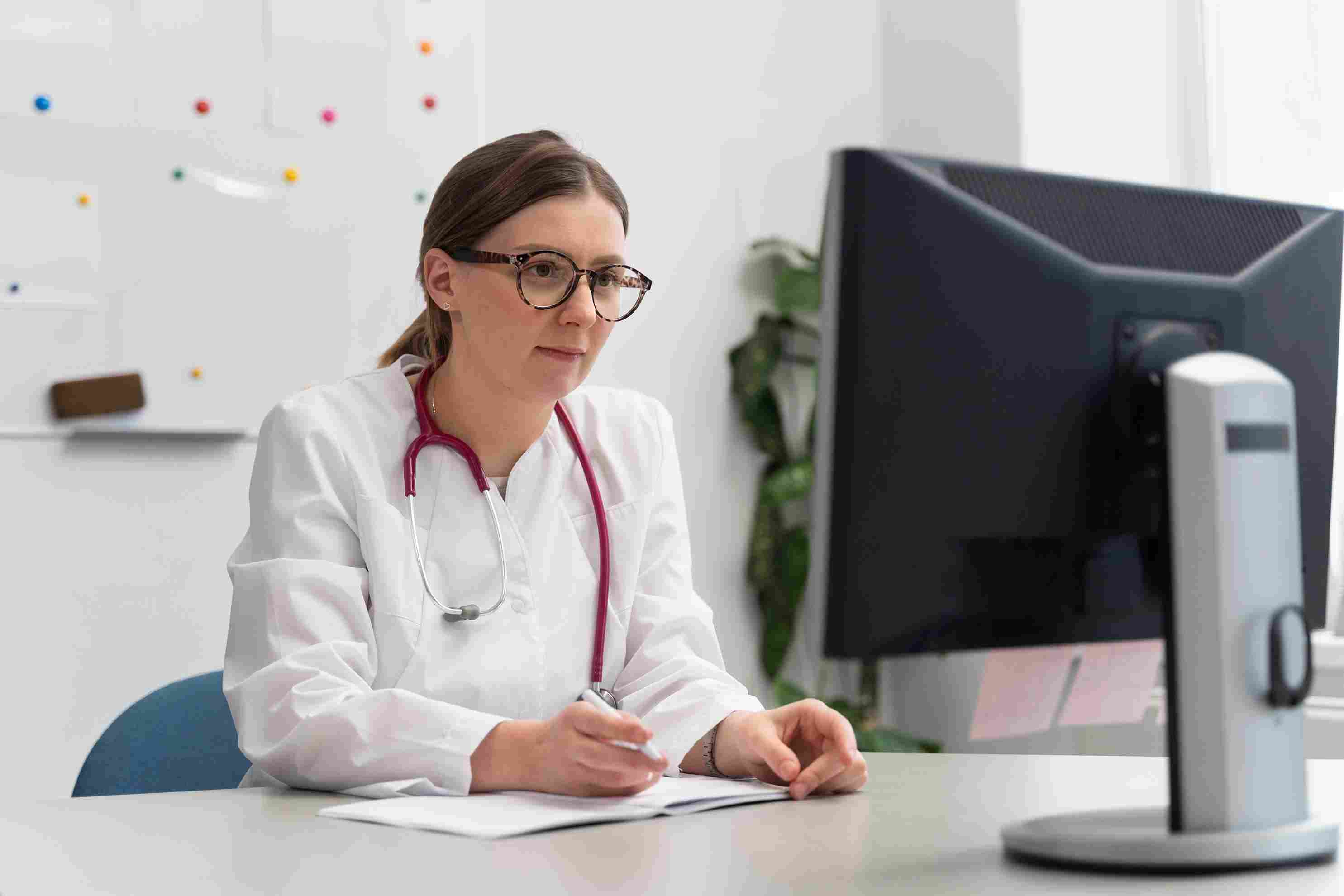 Female doctor sitting at a desk using a hospital management system on a desktop computer to review patient records and billing information