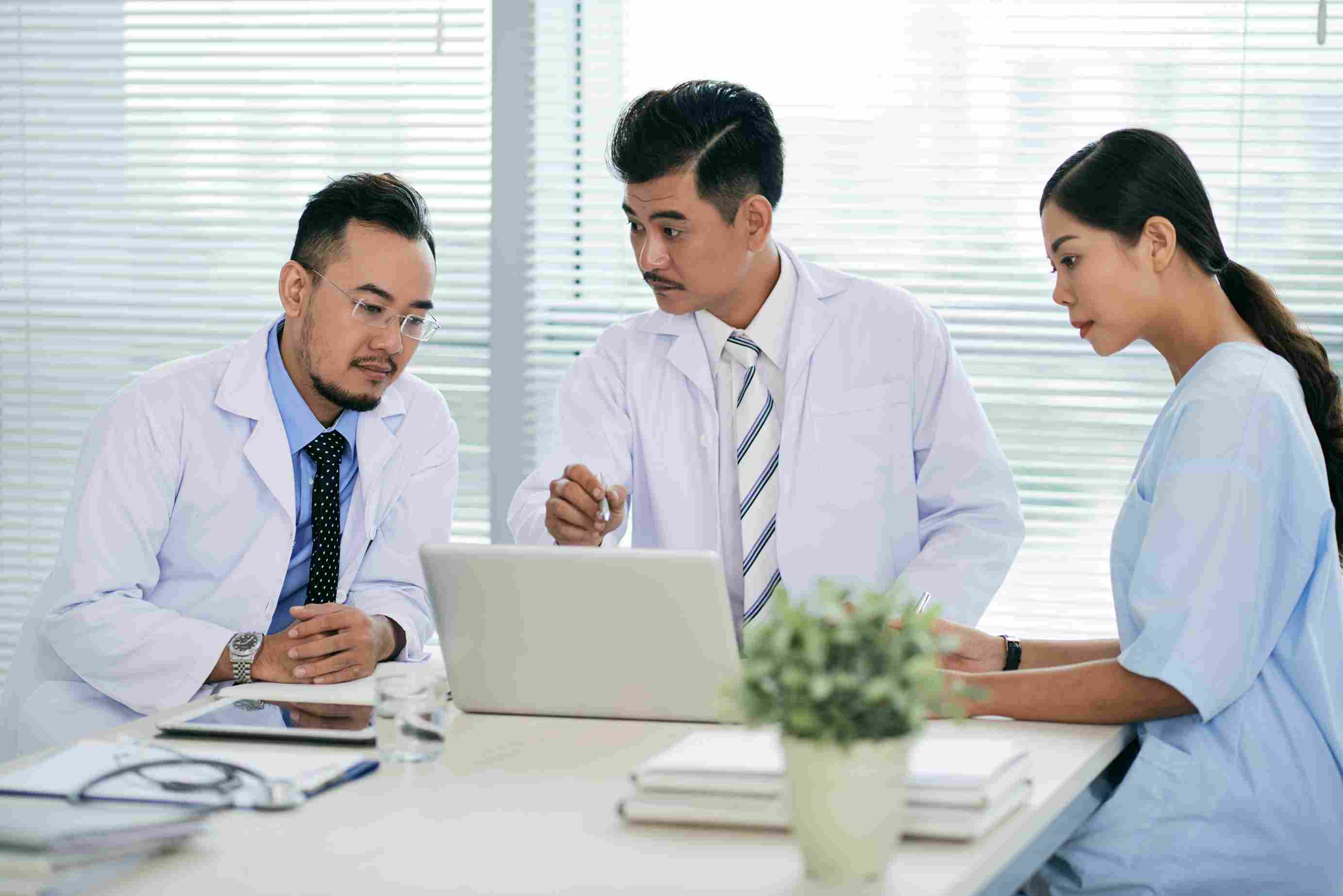 Group of doctors discussing at a laptop in a meeting room, symbolizing hospital planning and PhilHealth claims management