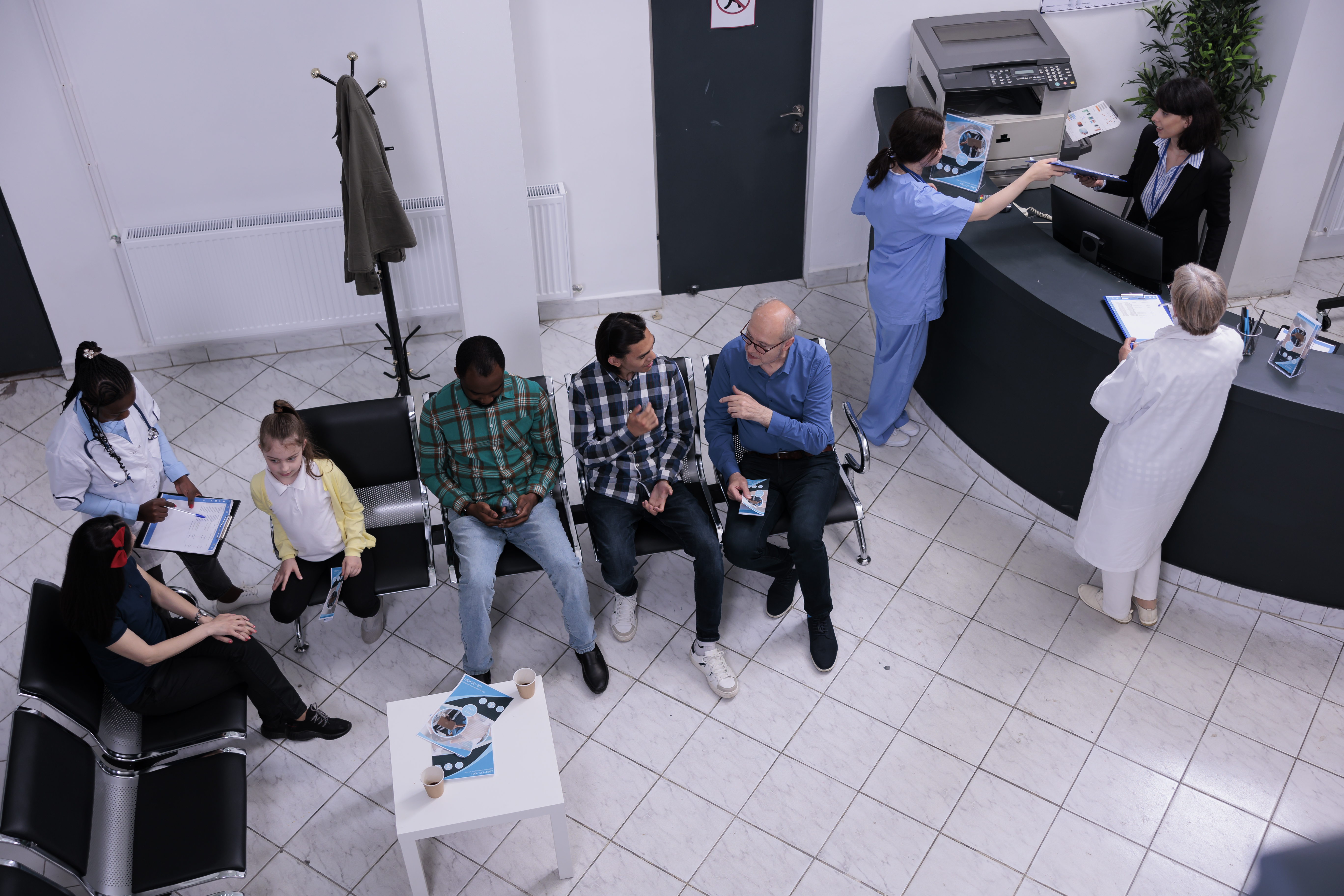 Top view of a hospital reception and waiting area where patients queue for appointments while staff manage registrations, illustrating the need for better workflow visibility