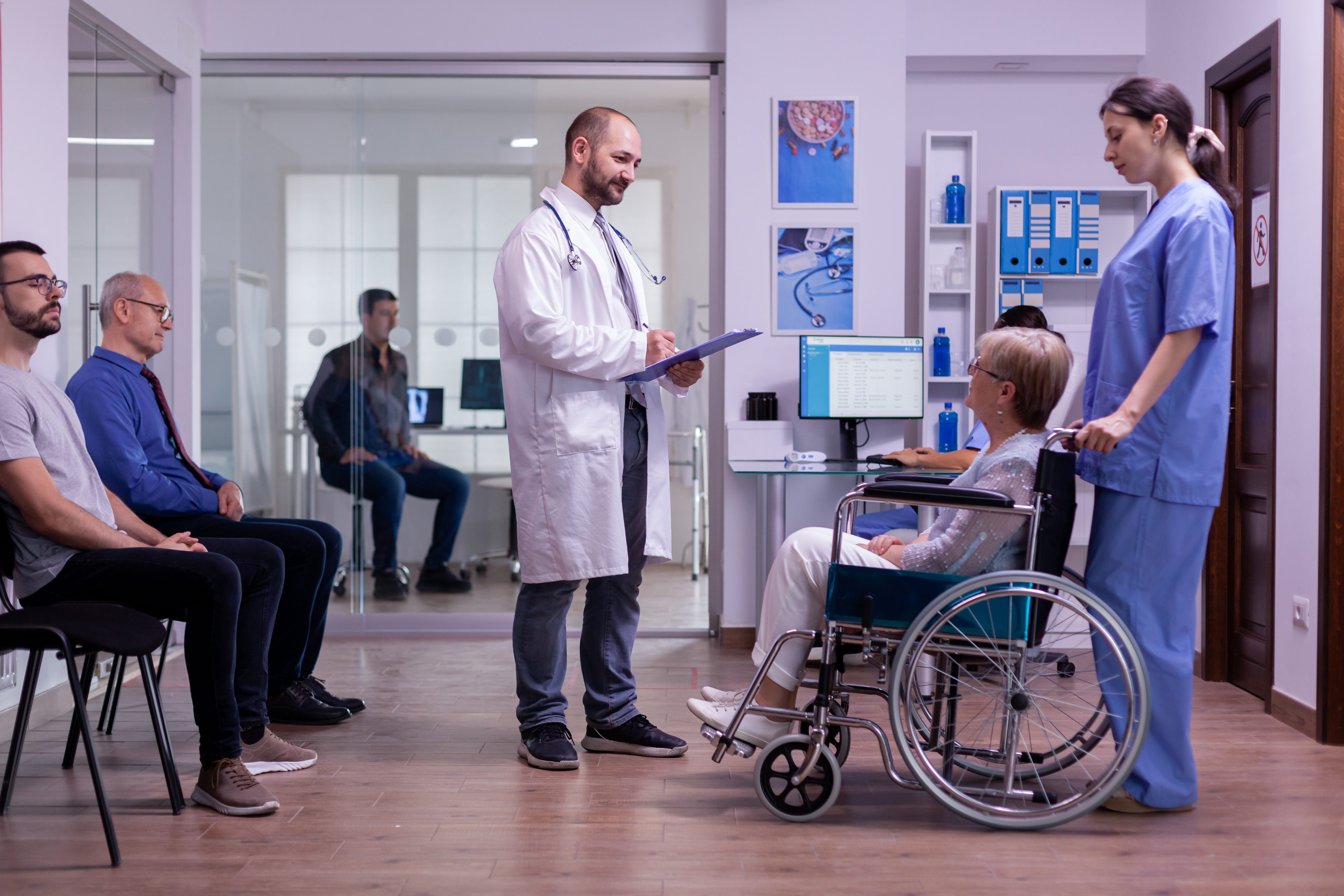 Patient in wheelchair talking to medical staff at a busy hospital reception area, representing how better workflow visibility can reduce queues and delays across OPD and discharge processes