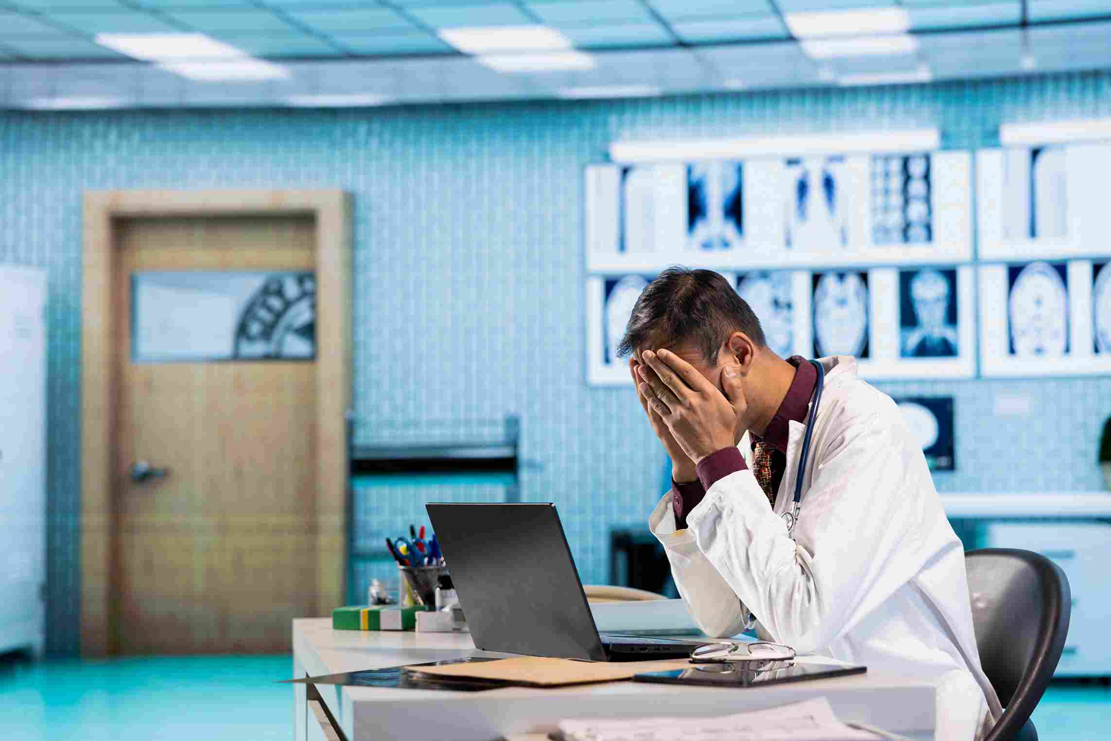Doctor overwhelmed by administrative burden showing signs of healthcare burnout at computer workstation