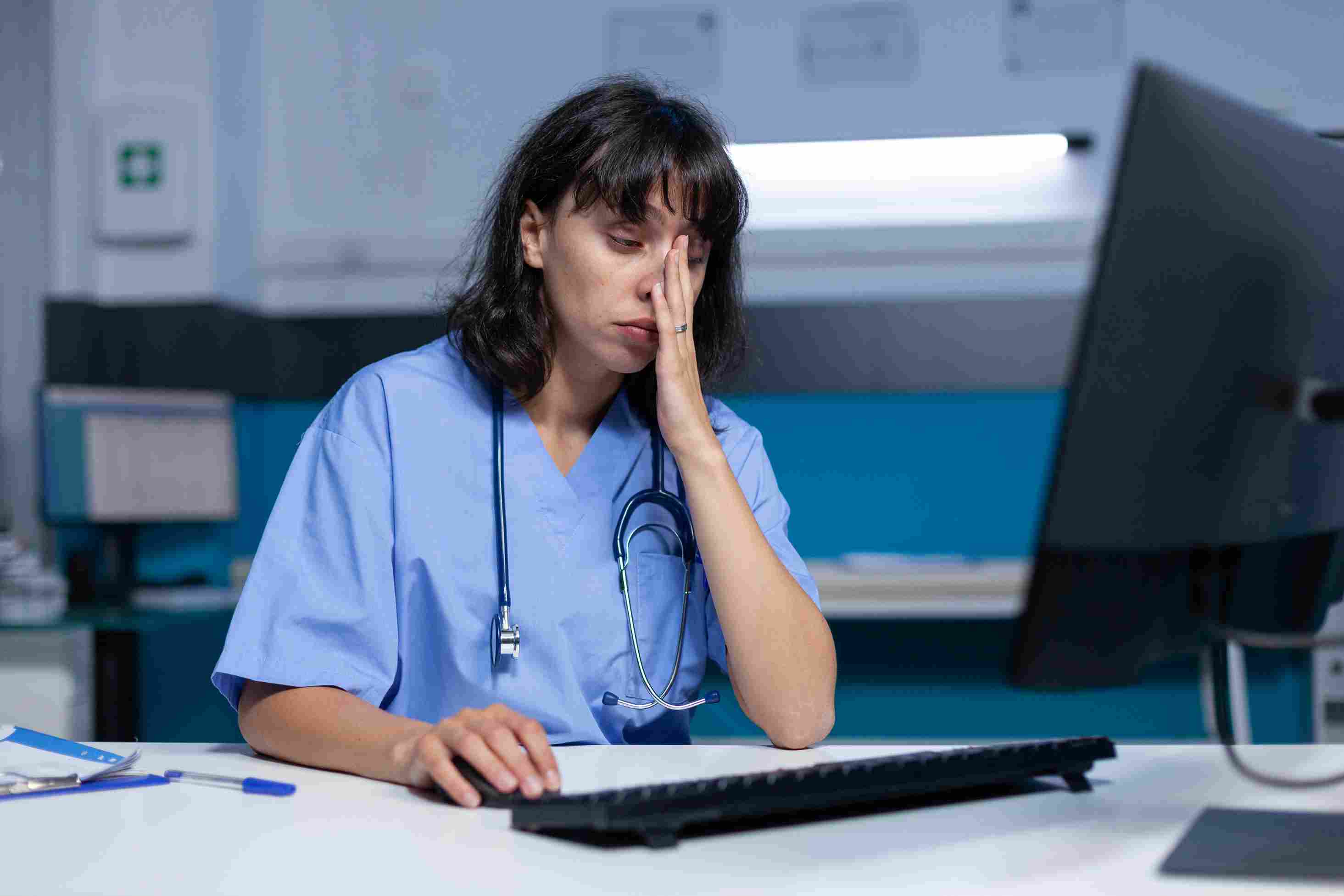 Tired nurse working late night shift experiencing fatigue while using hospital computer system