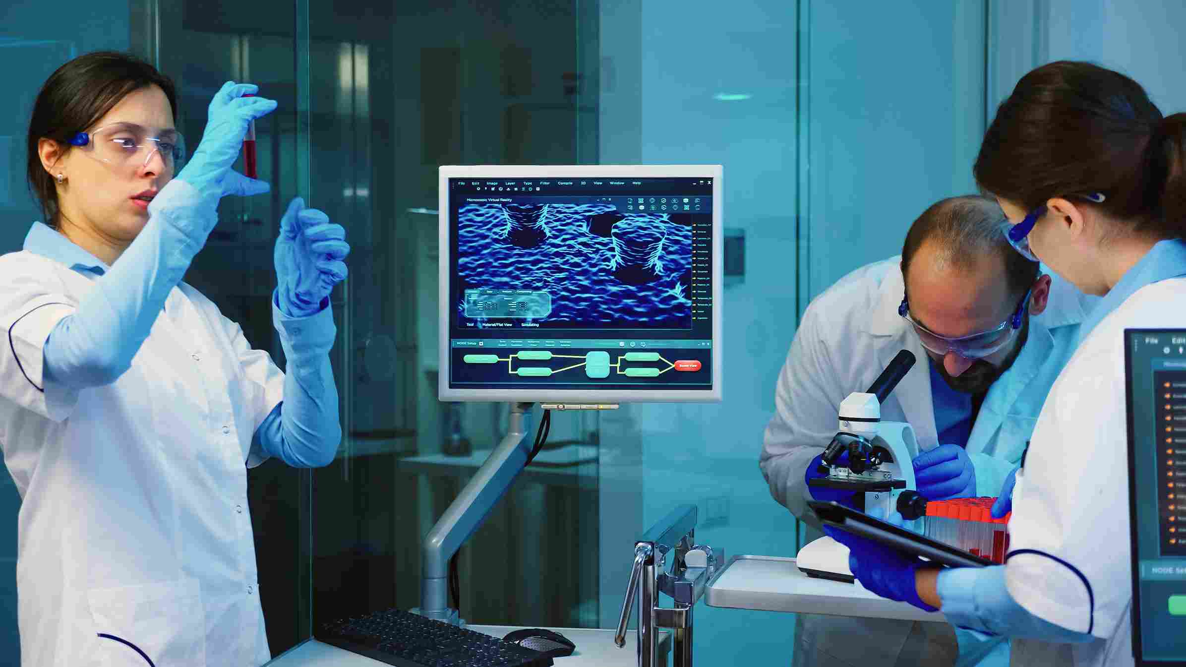 Senior chemist analyzing blood sample while laboratory team discusses test results using digital Laboratory Management Software