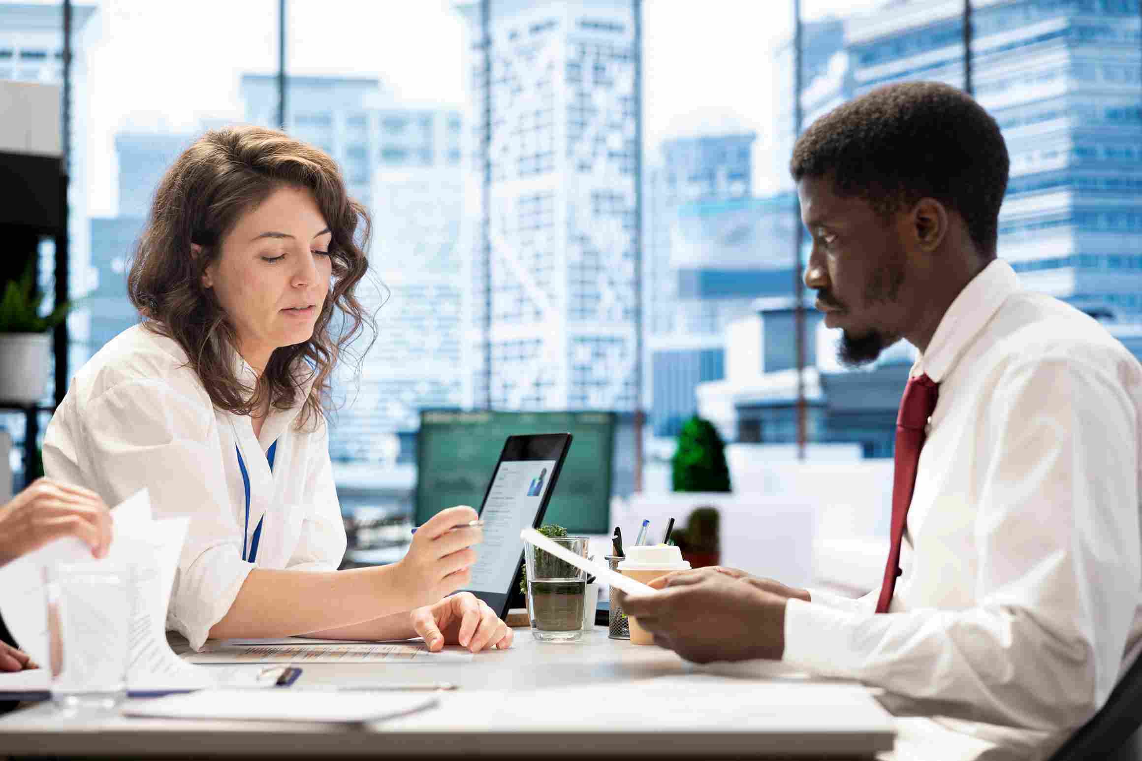 A hospital procurement officer and an HMS vendor representative sitting across a meeting table reviewing printed contract documents alongside a tablet displaying vendor information, representing the detailed contract review process where hospital leaders evaluate SLA terms, customisation clauses, hidden costs, and data portability guarantees before committing to a Hospital Management System