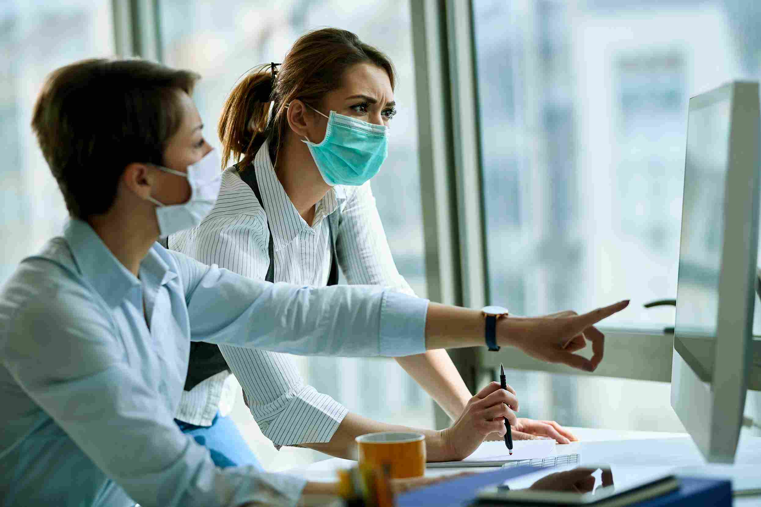 Two healthcare administrators wearing face masks reviewing financial performance data on a computer monitor, representing the process of measuring billing accuracy and revenue recovery after Hospital Management System implementation