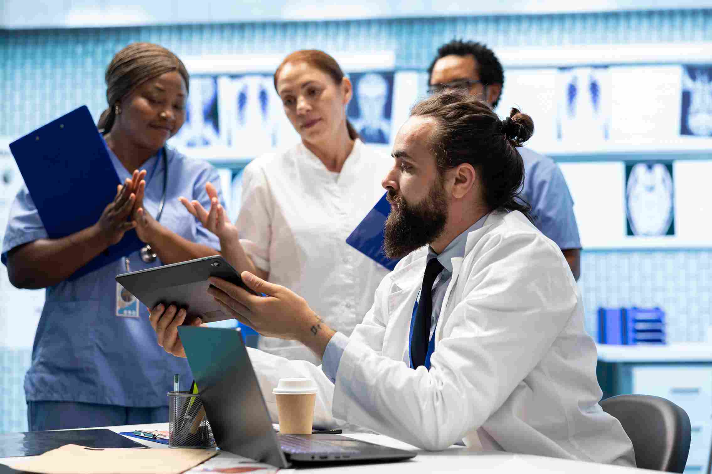A doctor in a white coat holding a tablet displaying a radiology scan and explaining it to a patient in a hospital room, representing how integrated HMS software gives clinical teams instant access to patient data and reduces diagnostic delays