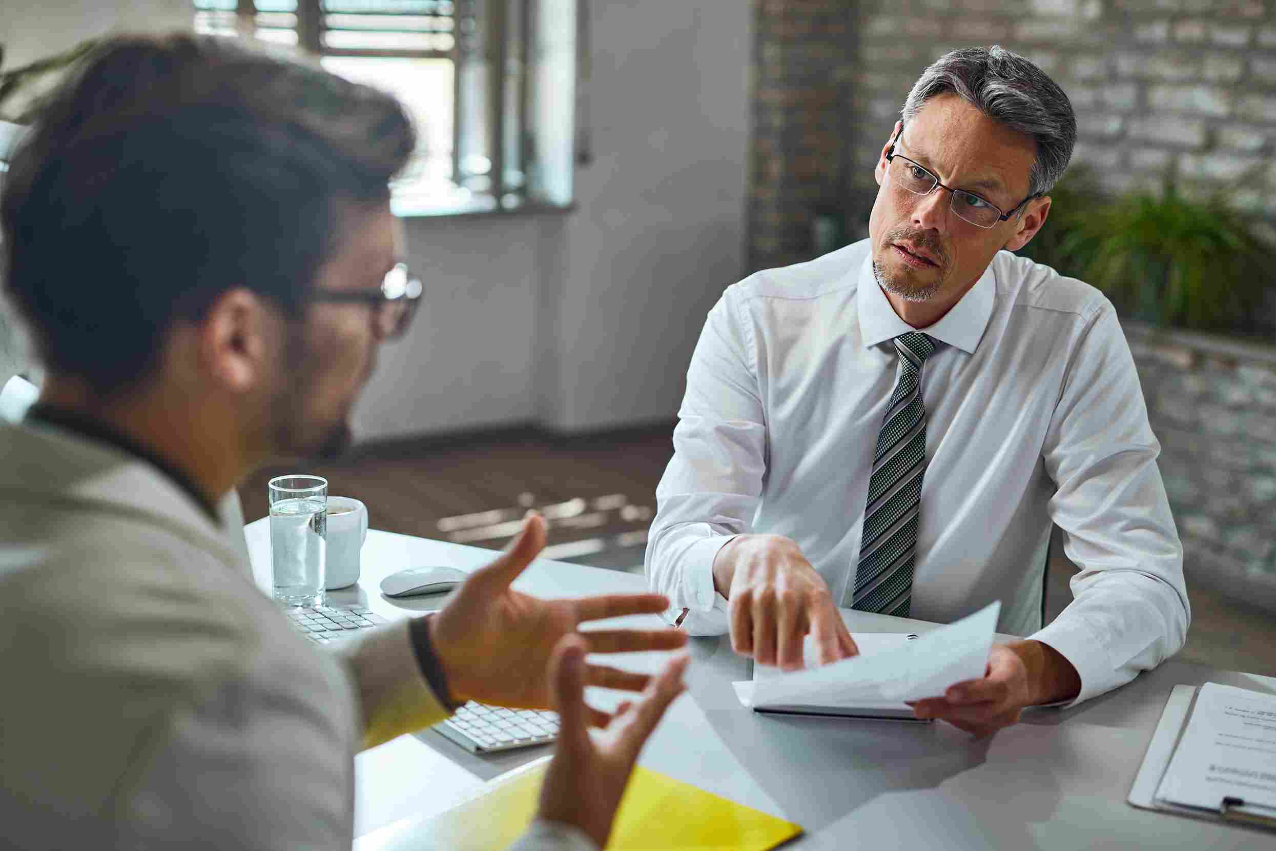 A senior hospital administrator in formal attire holding contract documents and listening carefully during a one on one meeting with an HMS vendor representative, representing the critical vendor evaluation process where hospital leaders ask hard questions about data ownership, SLA guarantees, and hidden costs before signing a Hospital Management System contract