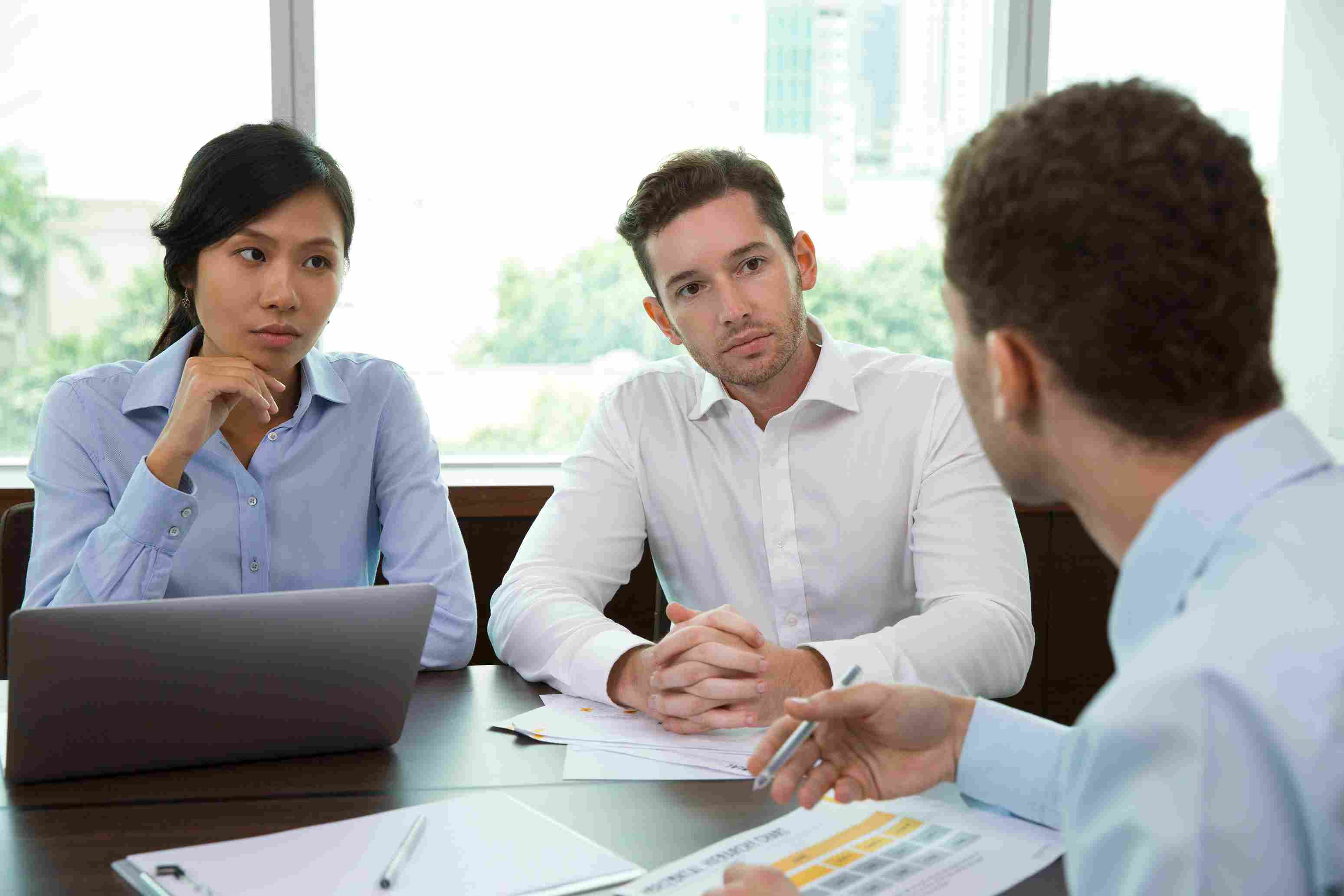 Two hospital decision makers sitting across a meeting table listening attentively with focused expressions as an HMS vendor representative explains contract terms and system capabilities, representing the critical pre-contract evaluation conversation where hospital owners ask specific questions about uptime SLAs, post go-live support, ABDM compliance, customisation costs, and data ownership before selecting a Hospital Management System vendor