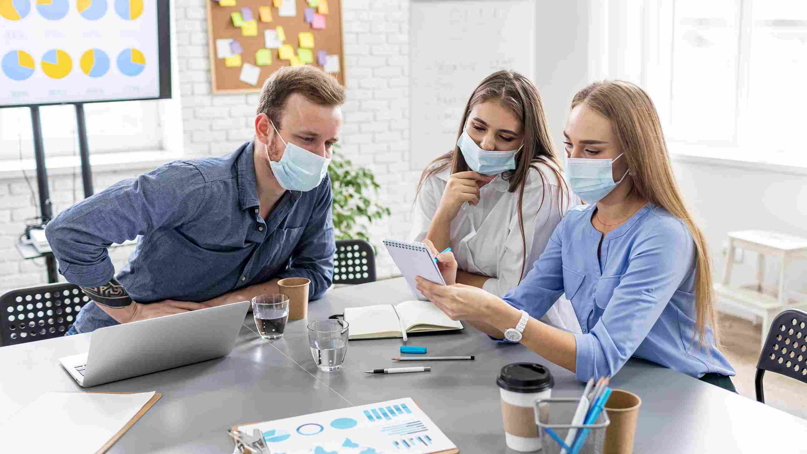 A hospital administrator and two medical staff members wearing face masks reviewing charts and notes at a meeting table with a laptop and data charts visible in the background, representing the internal planning and preparation required for ABDM integration and ABHA health record linkage in Indian hospitals in 2026