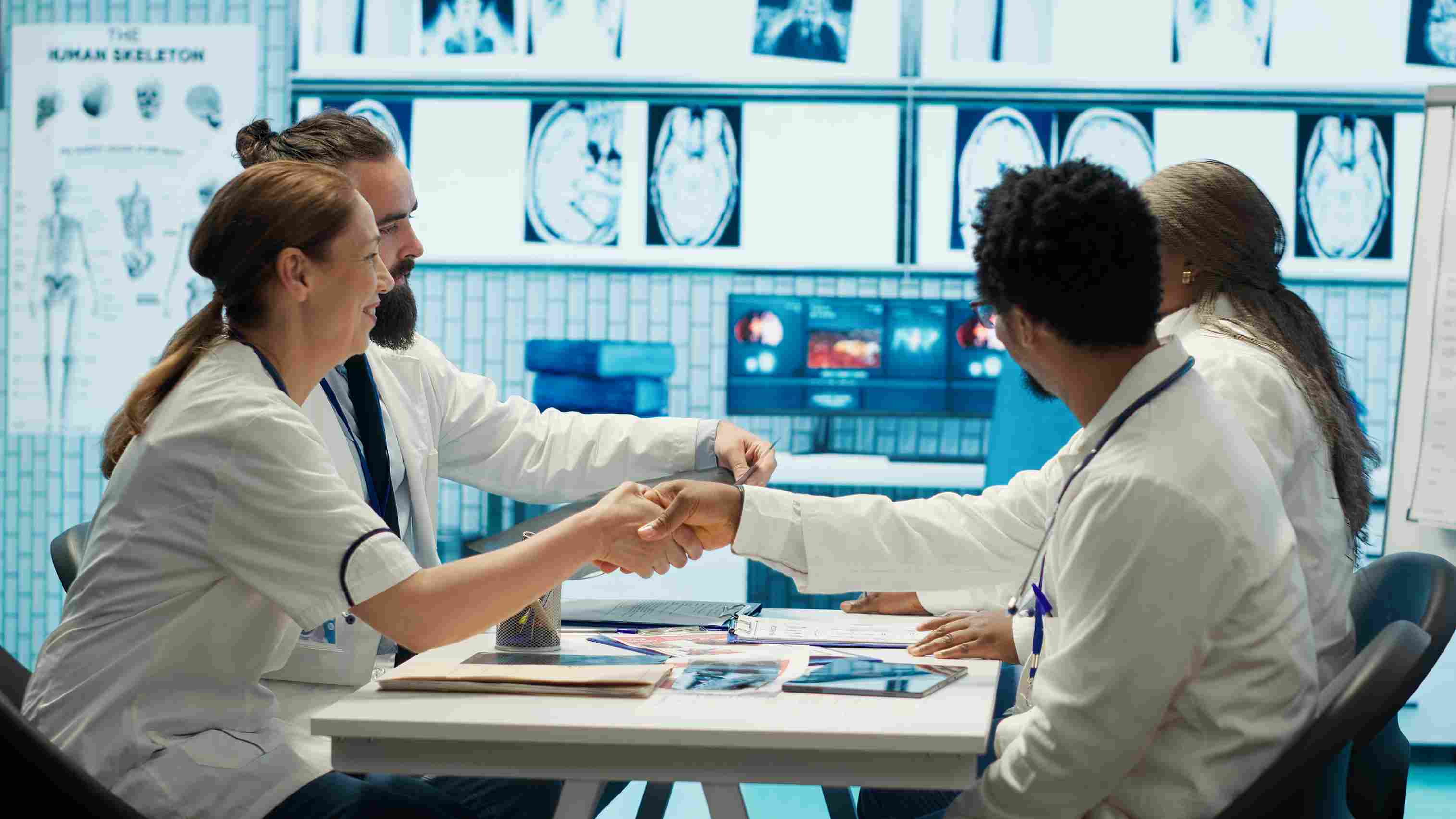 Two doctors in white lab coats shaking hands across a meeting table with medical imaging scans displayed on screens in the background, representing a hospital finalising its partnership with an ABDM compliant Hospital Management System vendor ahead of the 2026 integration deadline