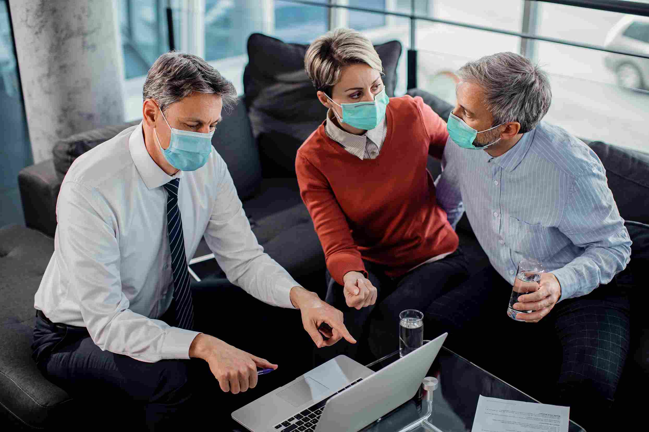 Three senior hospital administrators wearing face masks leaning over a laptop in an informal meeting setting, representing the executive level decision making process involved in preparing a hospital for Ayushman Bharat Digital Mission compliance and ABHA health record linkage requirements in 2026